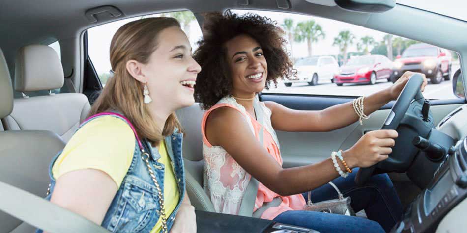 Two teenage girls sit in the front seat of a car, laughing
