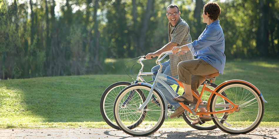 Two adults ride bikes together on a sunny day